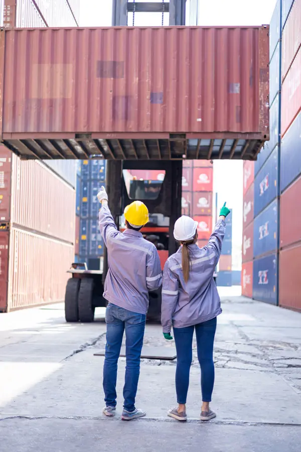 2 employees with hard hats pointing at shipping containers