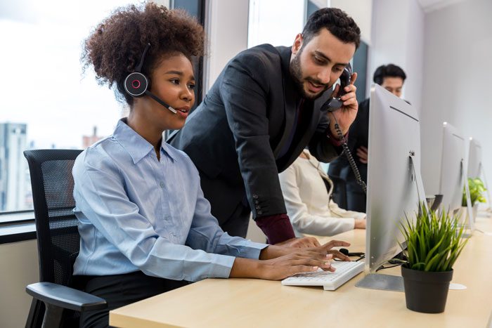 An agent taking a call in an office with a manager listening in as well. 