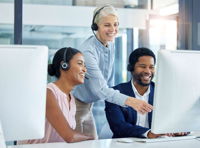 a group of employees at desks going over something on a monitor and smiling