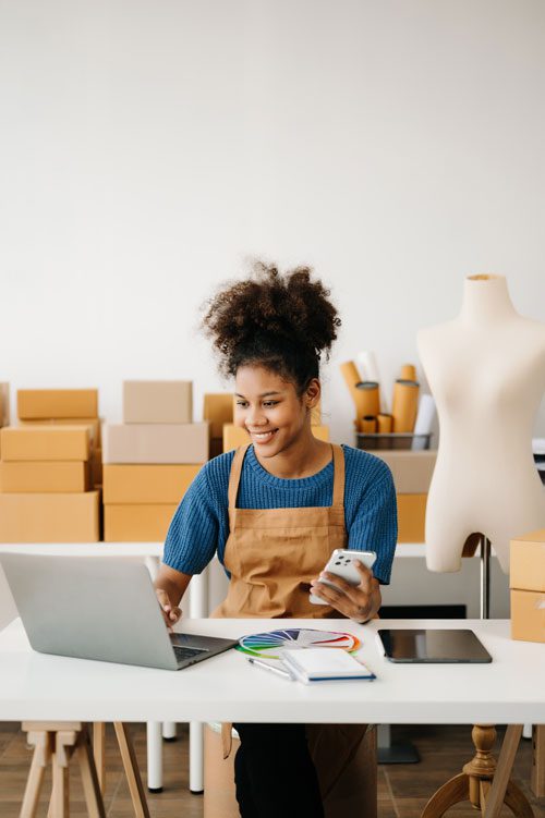 a young small business owner smiling and doing e-commerce work on laptop