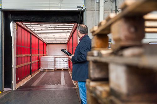 an employee with a checklist reviewing shipping pallets being loaded into a mostly empty container