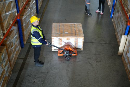 an employee in a warehouse loading a  pallet onto a pallet jack