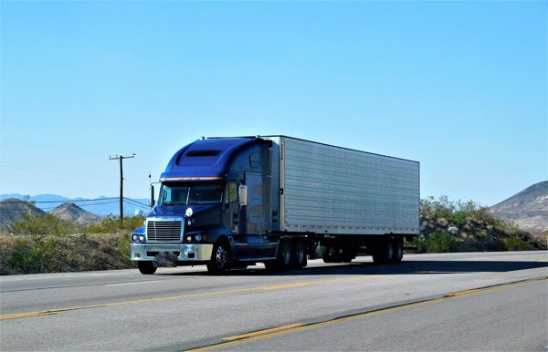 blue semi-truck with a loaded trailer on highway